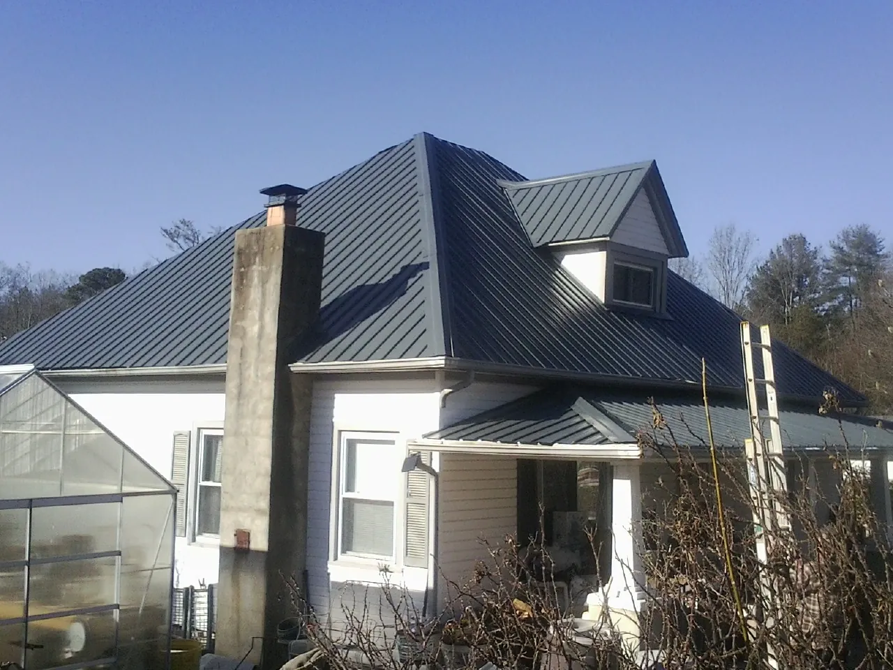 Dark blue standing seam metal roof on a white farmhouse with dormer — Slate & Tile Roof Repair by Roofing Brothers in Dobson