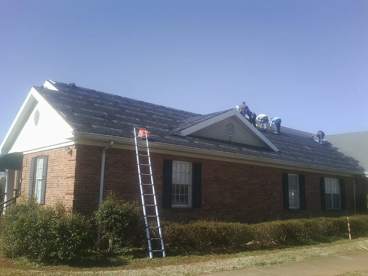 Crew tearing shingles off a brick ranch roof with a ladder set — Metal Roof Repair work by our crew in Dobson