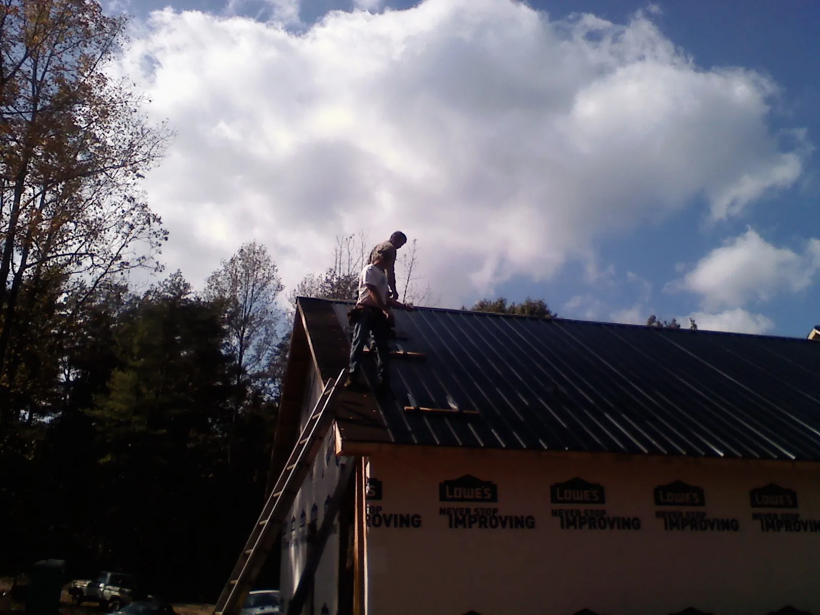 Roofer fastening dark metal panels high against a cloudy sky, from a Roof Inspection job in Dobson