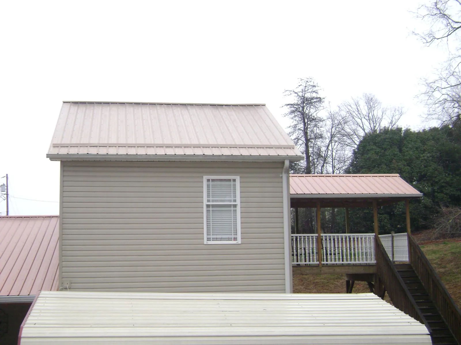 Tan metal roofs on a two story addition and attached porch, from a Roof Replacement job in Dobson